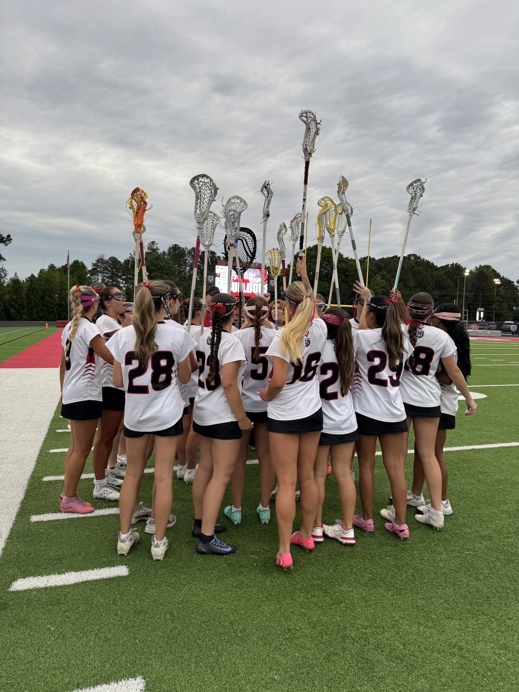 North Gwinnett girls lacrosse team huddle with sticks raised